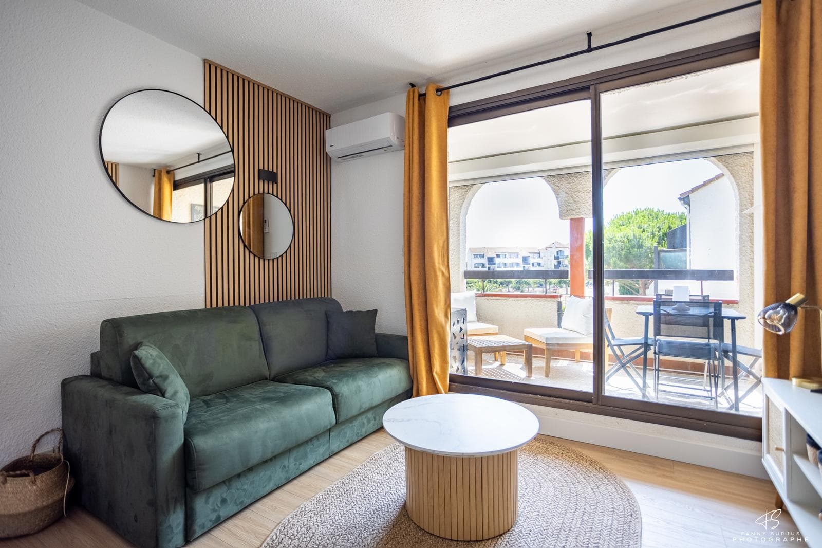 Salon du Duplex T2, canapé vert et ouverture sur le balcon à arcades